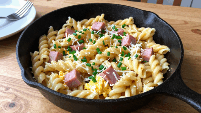 Schinkennudeln mit Ei und Schnittlauch in einer großen Pfanne auf dem Küchentisch