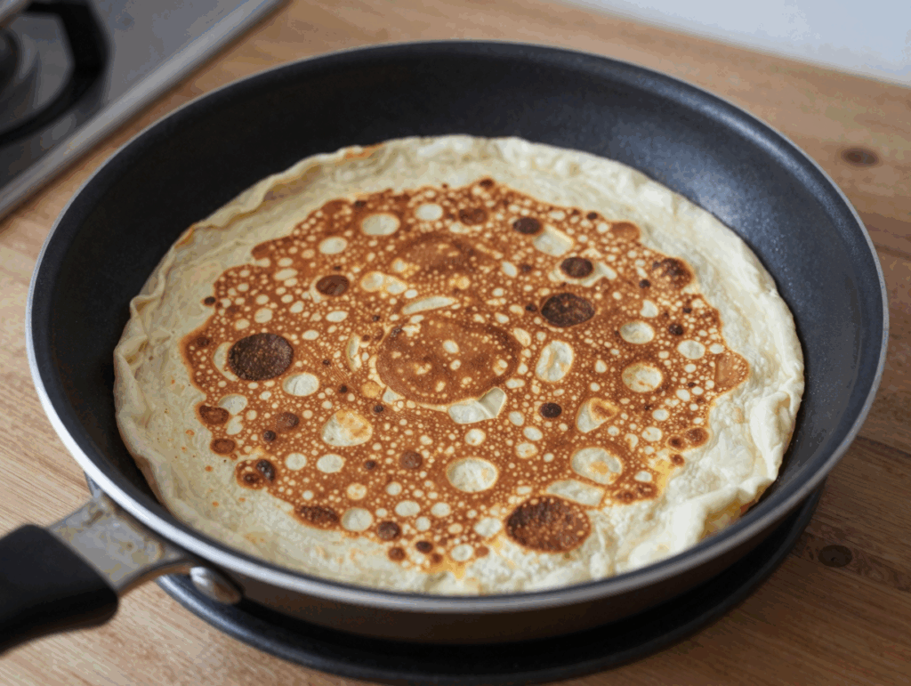 Dünner Pfannkuchen in der Pfanne kurz vor dem Wenden