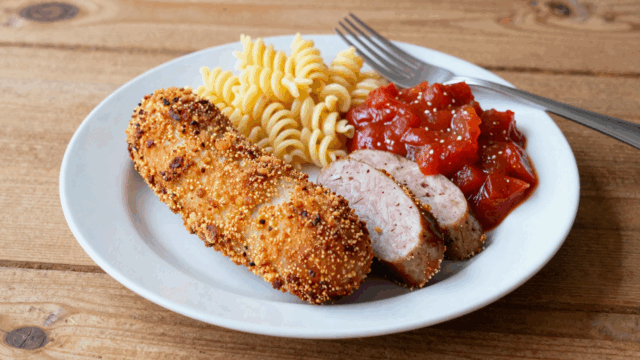 Panierte Jagdwurstscheiben mit Tomatensoße und Spirelli auf einem weißen Teller