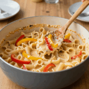 One-Pot-Nudeln mit Paprikastreifen in cremiger Soße im breiten Topf, ein Holzlöffel hebt eine Portion heraus
